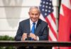 Iran Stakes: Trump Bets On Netanyahu Man in suit seated at a signing table