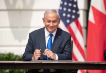 Iran Stakes: Trump Bets On Netanyahu Man in suit seated at a signing table
