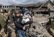 Border Market Inferno – 150+ Gone Rescuers carry a baby in a stroller through a destroyed bridge