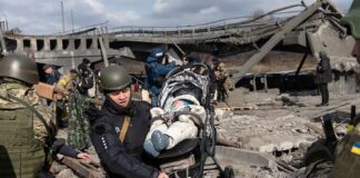 Rescuers carry a baby in a stroller through a destroyed bridge