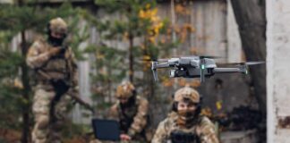 Quadcopter drone flying near camouflaged soldiers outdoors