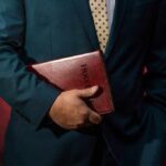 Church Leaders Moved Predators – For Years Person in a suit holding a red leather Bible