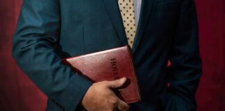 Person in a suit holding a red leather Bible