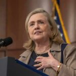 Hollywood Call Sparks Clinton Backlash woman speaking at a podium with microphone and flags behind