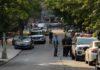 Homecoming Horror – Dozens Down, Killers Loose Police officers secure a residential street with patrol cars and yellow tape