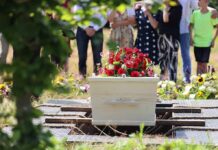 Teen Sits Up in Coffin During Her Own Wake White coffin with red flowers at outdoor burial