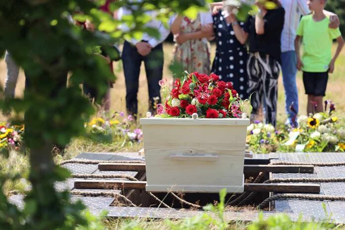 shutterstock_2368329541-1 White coffin with red flowers at outdoor burial