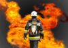 Firefighter in protective gear facing large flames