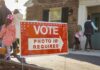 Governor Demands Answers On Dan Sullivan Double Red voting sign with arrow near people entering a polling place