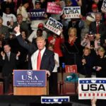 Donald Trump addresses a rally crowd at a podium, raising his fist