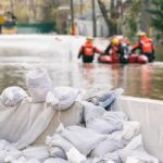 Storm Rachel’s Rage, Children Swept Away Sandbags stacked near a flooded street with rescue workers in a boat