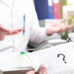 A Campaign Absence Draws Fresh Questions About Timing Doctor gesturing during consultation with patient holding paper with question mark