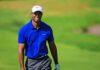 Comeback Whispers Swirl – Tiger Stays Silent Tiger Woods smiling on a golf course in a blue polo