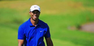 Tiger Woods smiling on a golf course in a blue polo