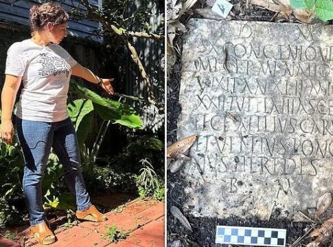A woman in a garden pointing at a Roman inscription on a stone slab surrounded by greenery