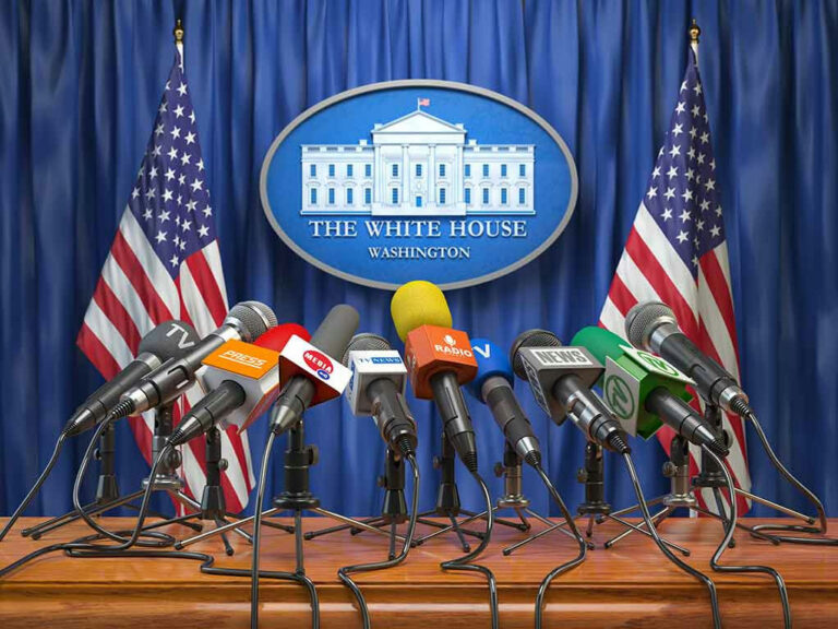 White House podium with multiple microphones and flags.
