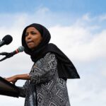 Woman in hijab speaking at podium with microphones.