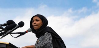 Woman in hijab speaking at podium with microphones.