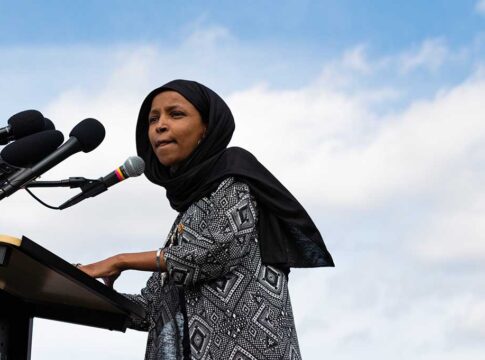 Woman in hijab speaking at podium with microphones.