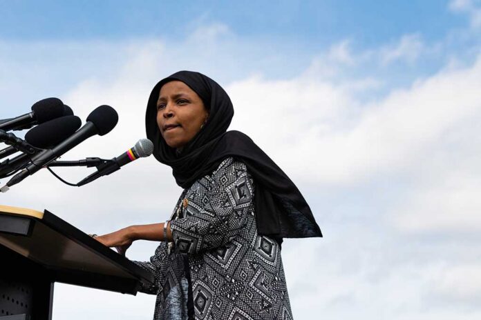 Woman in hijab speaking at podium with microphones.