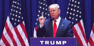 Politician speaking at podium with American flags behind.