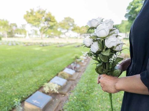 Person holding white roses at a cemetery.