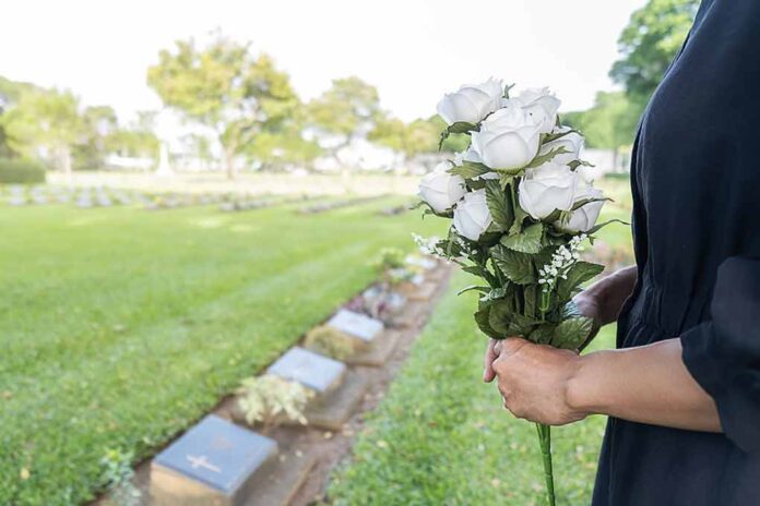 Person holding white roses at a cemetery.