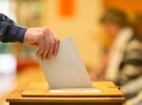 A hand placing a ballot into a ballot box during an election