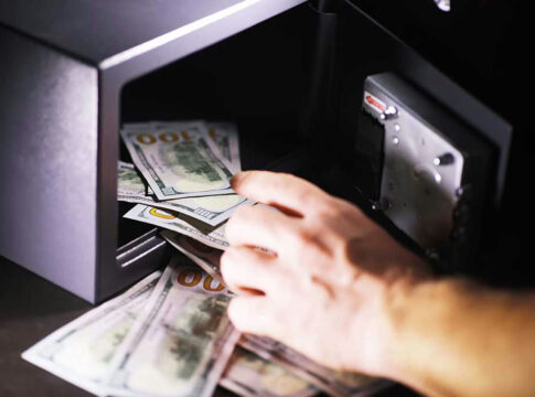Hand placing cash into open safe.