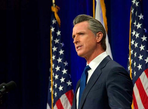 Man speaking at podium with American flags behind him.
