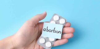 Hand holding pills labeled "abortion" on blue background.