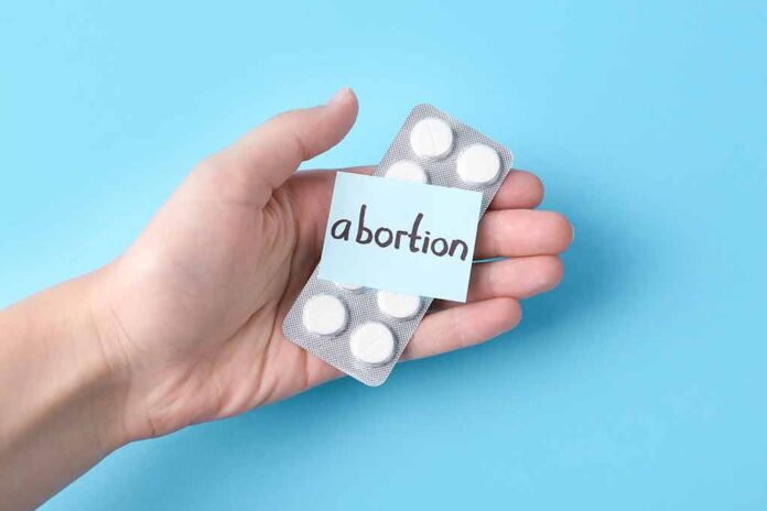 Hand holding pills labeled "abortion" on blue background.