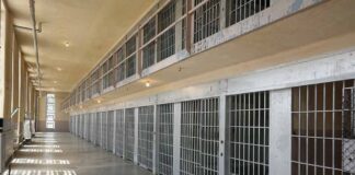 Empty prison cell block with barred doors and walkway.