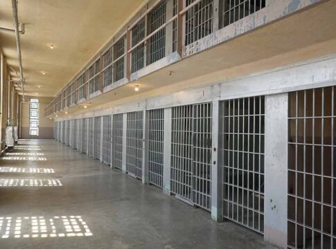 Empty prison cell block with barred doors and walkway.