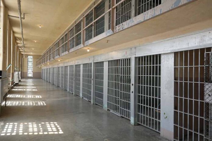 Empty prison cell block with barred doors and walkway.