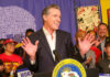 Man speaking at podium with smiling audience behind.