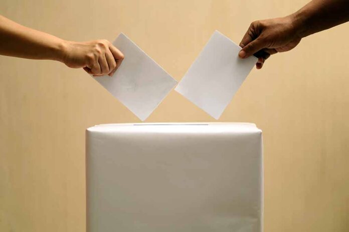 2395285153 featured image Two hands placing ballots into a voting box.