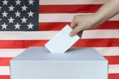 Hand casting ballot into box before U.S. flag