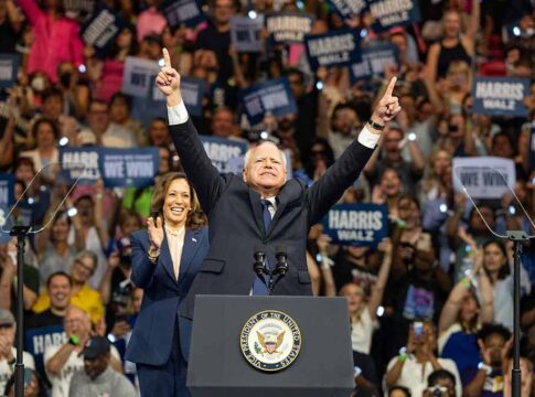 Politicians at a rally, crowd in the background cheering.