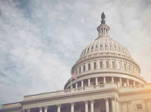 US Capitol dome with American flag and cloudy sky.