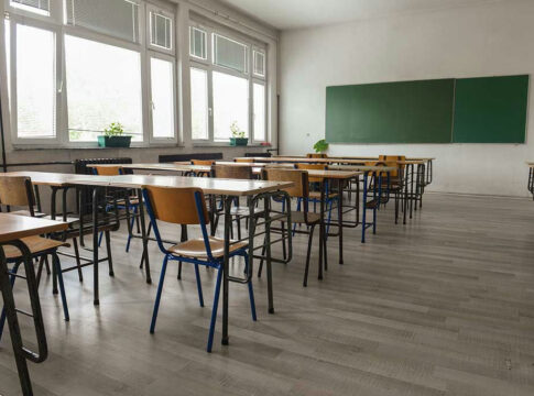 Empty classroom with desks, chairs, windows, and chalkboard.