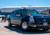 A black presidential limousine parked at an airport with Air Force One in the background.