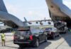 Military aircraft unloading vehicles at an airport with security personnel present
