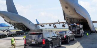 Military aircraft unloading vehicles at an airport with security personnel present
