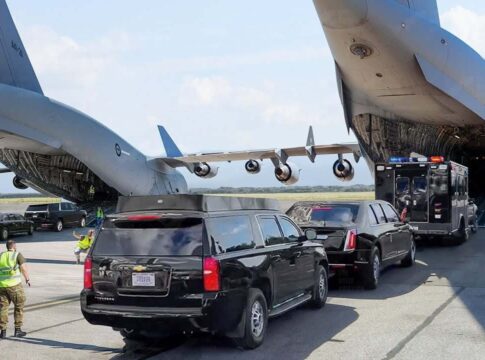 Military aircraft unloading vehicles at an airport with security personnel present