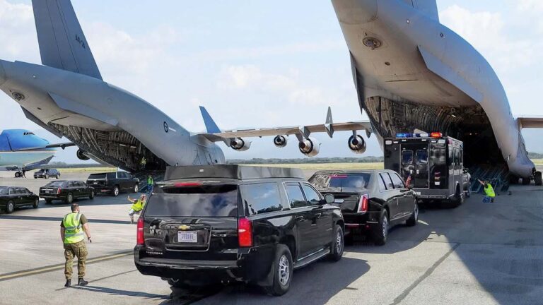 Military aircraft unloading vehicles at an airport with security personnel present