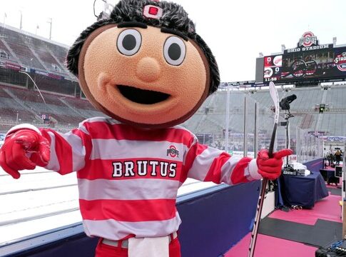 Brutus Buckeye mascot celebrating at a sports event in a stadium