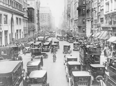 A busy city street from 100 years ago filled with vintage cars and crowds of people