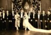 A vintage wedding photo featuring a bride and groom surrounded by their wedding party in formal attire
