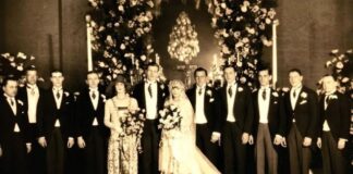 A vintage wedding photo featuring a bride and groom surrounded by their wedding party in formal attire
